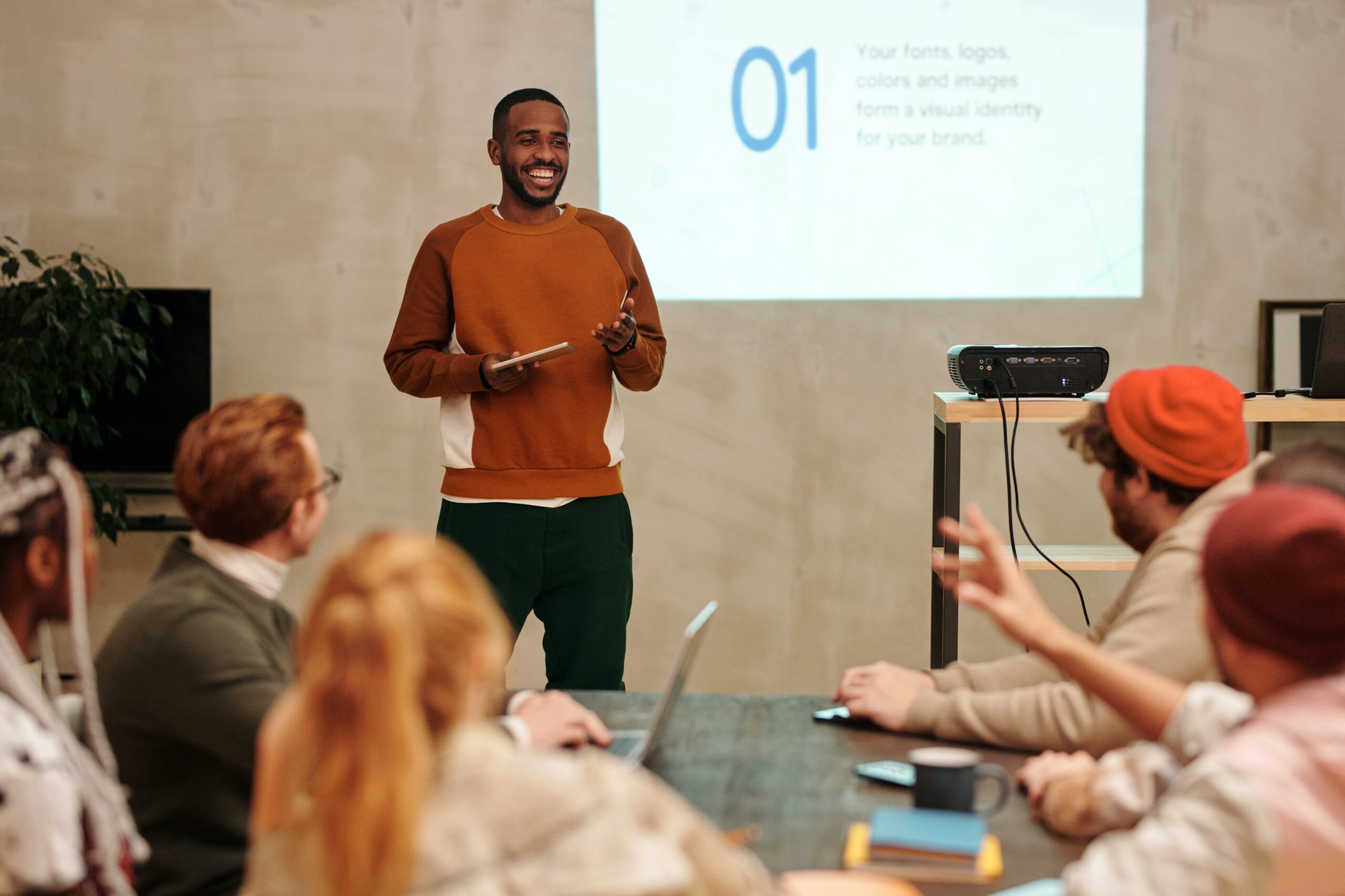 A man smiling while giving a presentation to a group of people.