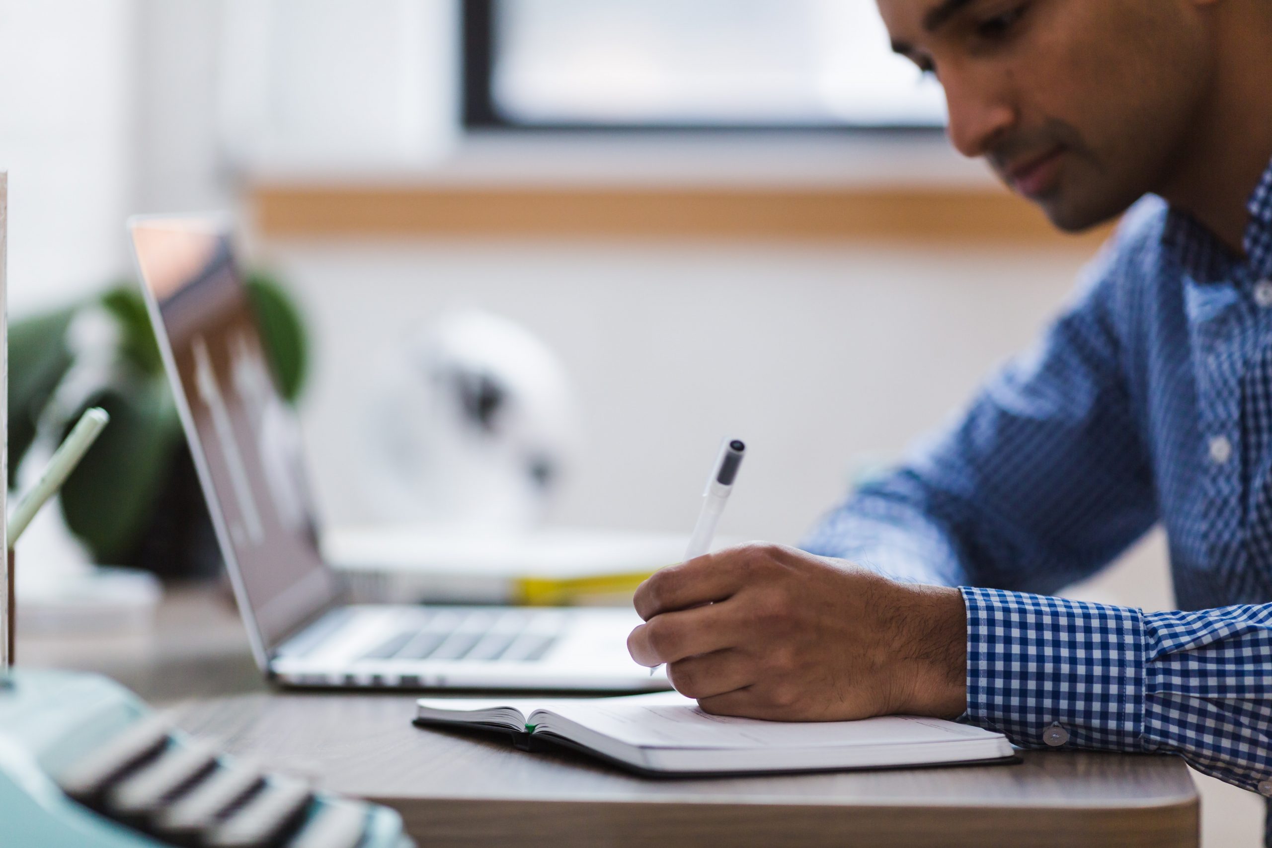 Man takes notes on paper from the laptop sitting next to him.