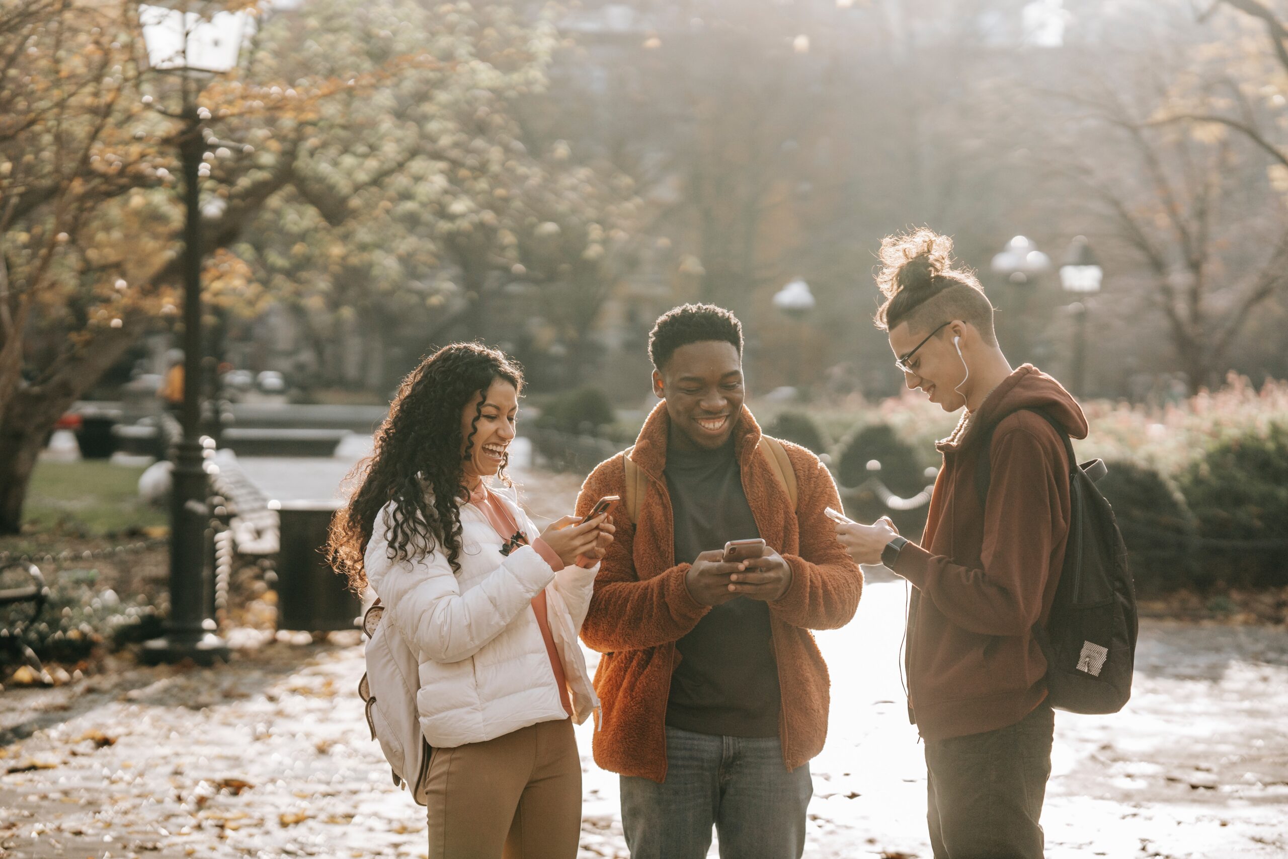 A group of friends standing outside, all looking at their phones.