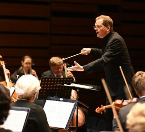 A man in black conducting an orchestra